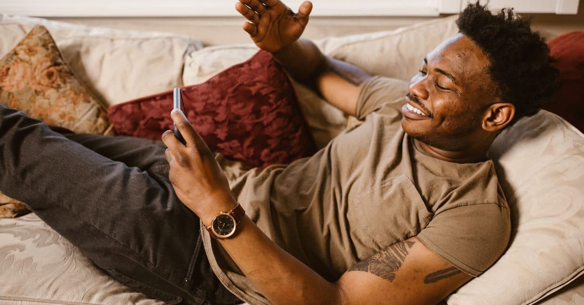 Homme allongé sur un canapé regardant un flux IPTV sur son smartphone Android
